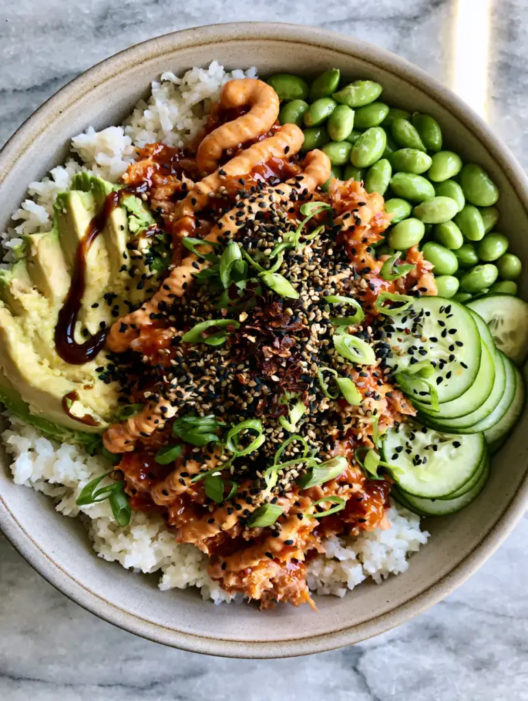 Close up of glossy sriracha-coated tuna and sliced avocado in a matte grey bowl. (Tuna Rice Bowl)