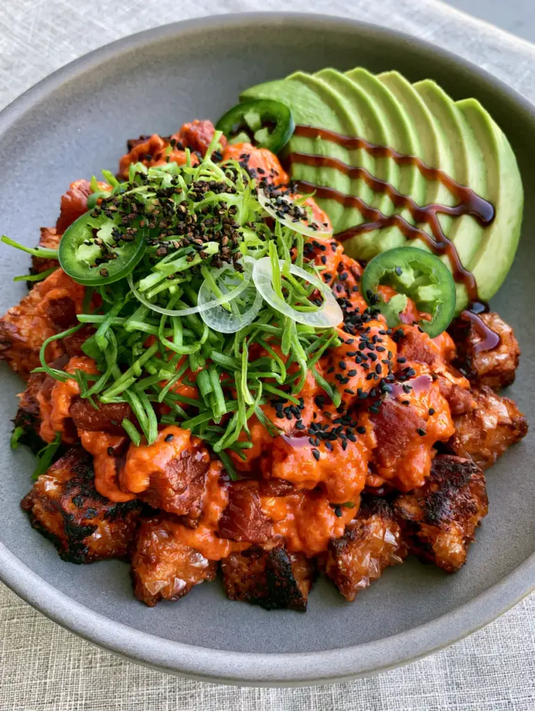 Detailed shot of a tuna crispy rice bowl with fanned avocado, jalapeño slices, and a dark amber unagi sauce drizzle.