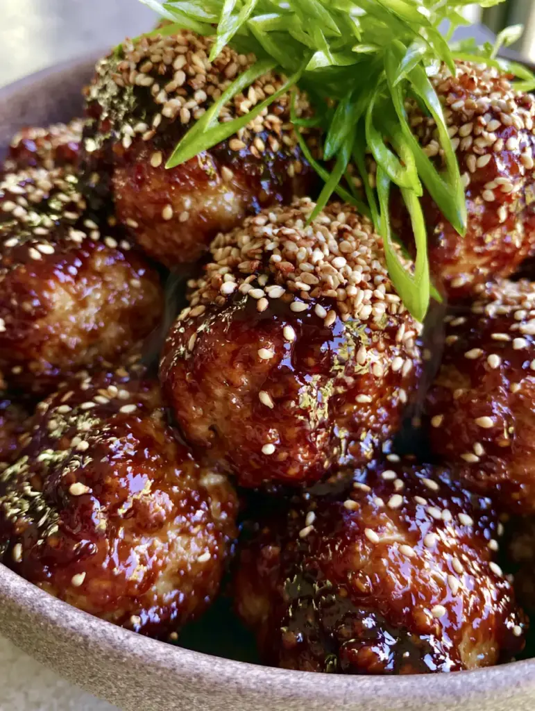 Handheld smartphone photo of juicy Asian chicken meatballs with steam rising and vibrant green scallion garnishes.