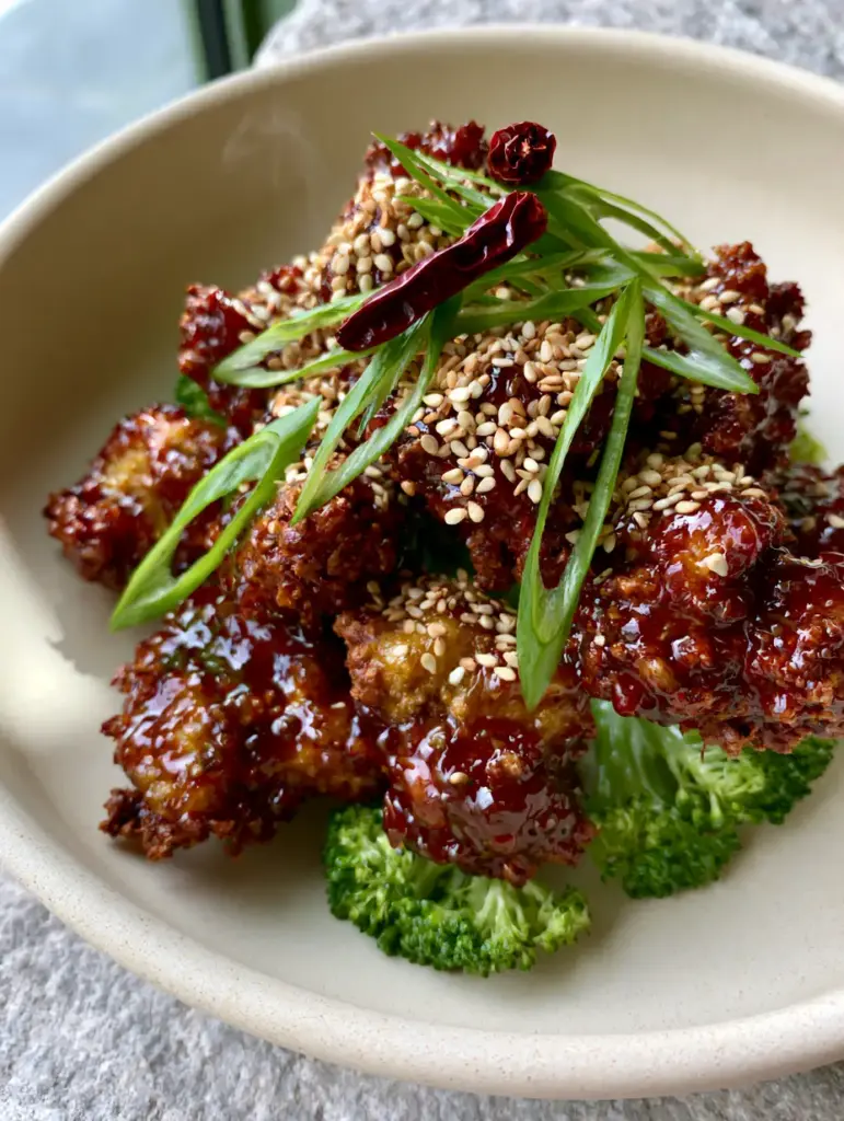 Extreme close-up of craggy air-fried chicken coated in a translucent mahogany glaze. (general tso's chicken)