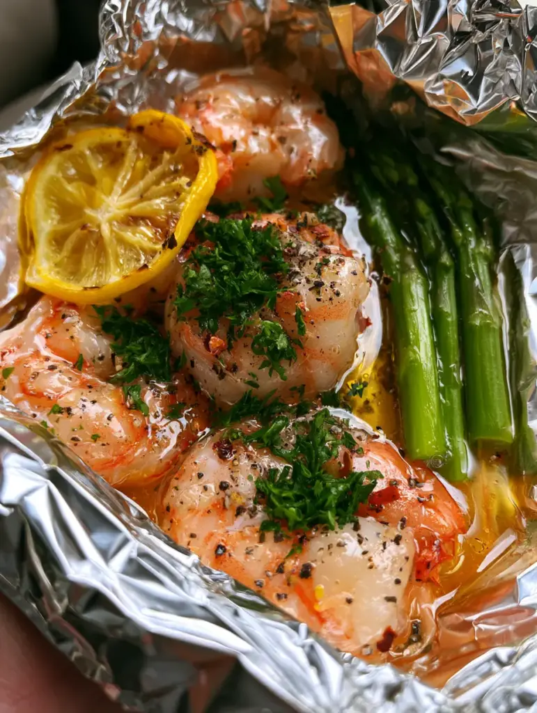 A steaming silver foil packet filled with pink shrimp, charred lemon slices, and green asparagus.