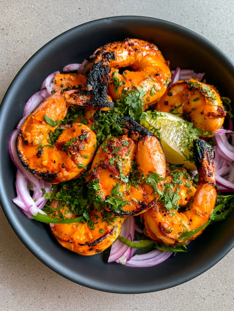 Macro view of jumbo tandoori prawns coated in a thick orange marinade with cracked black pepper and dried fenugreek.