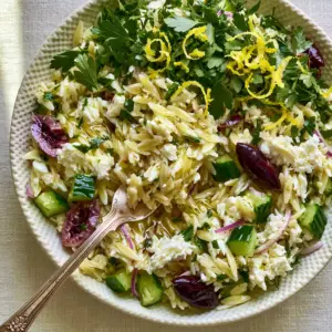 Extreme close-up of Mediterranean Orzo Salad with glistening vinaigrette and a vintage fork lifting a bite.