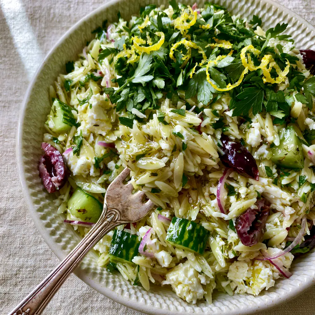 Mediterranean Orzo Salad with Lemon Herb Vinaigrette 1 Mediterranean Orzo Salad in an off-white bowl showing rustic feta crumbles and curled lemon zest.