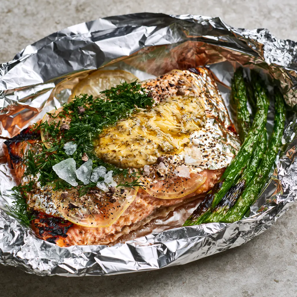 Grilled Salmon in Foil with Garlic Herb Butter and Charred Asparagus 1 Close-up of translucent lemon slices and fresh dill on top of a pink grilled salmon fillet.
